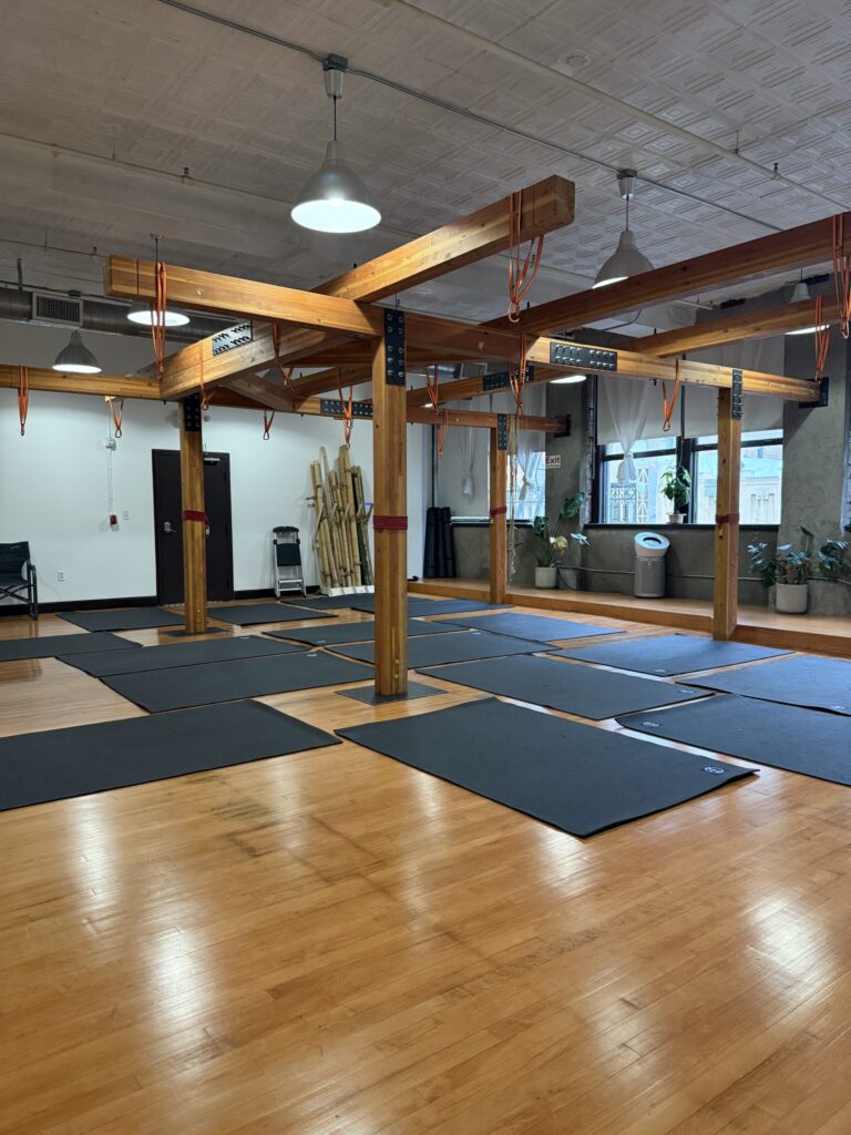 mats laid out on the expansive studio floor below our large wooden suspension frame with climbing straps and carabiners above each one, perfect for your next suspension or aerials class rental